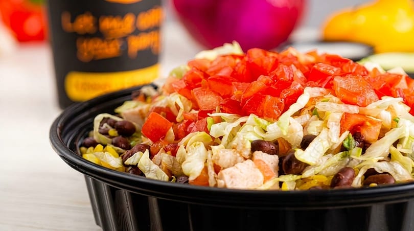 A close-up of a black bowl filled with a colorful salad, featuring diced tomatoes, lettuce, black beans, corn, and chicken.