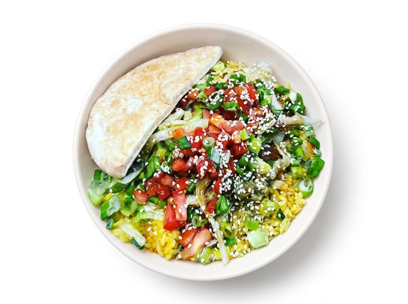 Bowl of yellow rice topped with tomatoes, green onions, sesame seeds, and pita bread.