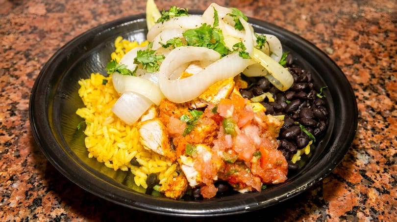 A black bowl filled with yellow rice, black beans, chicken, pico de gallo, and onions.