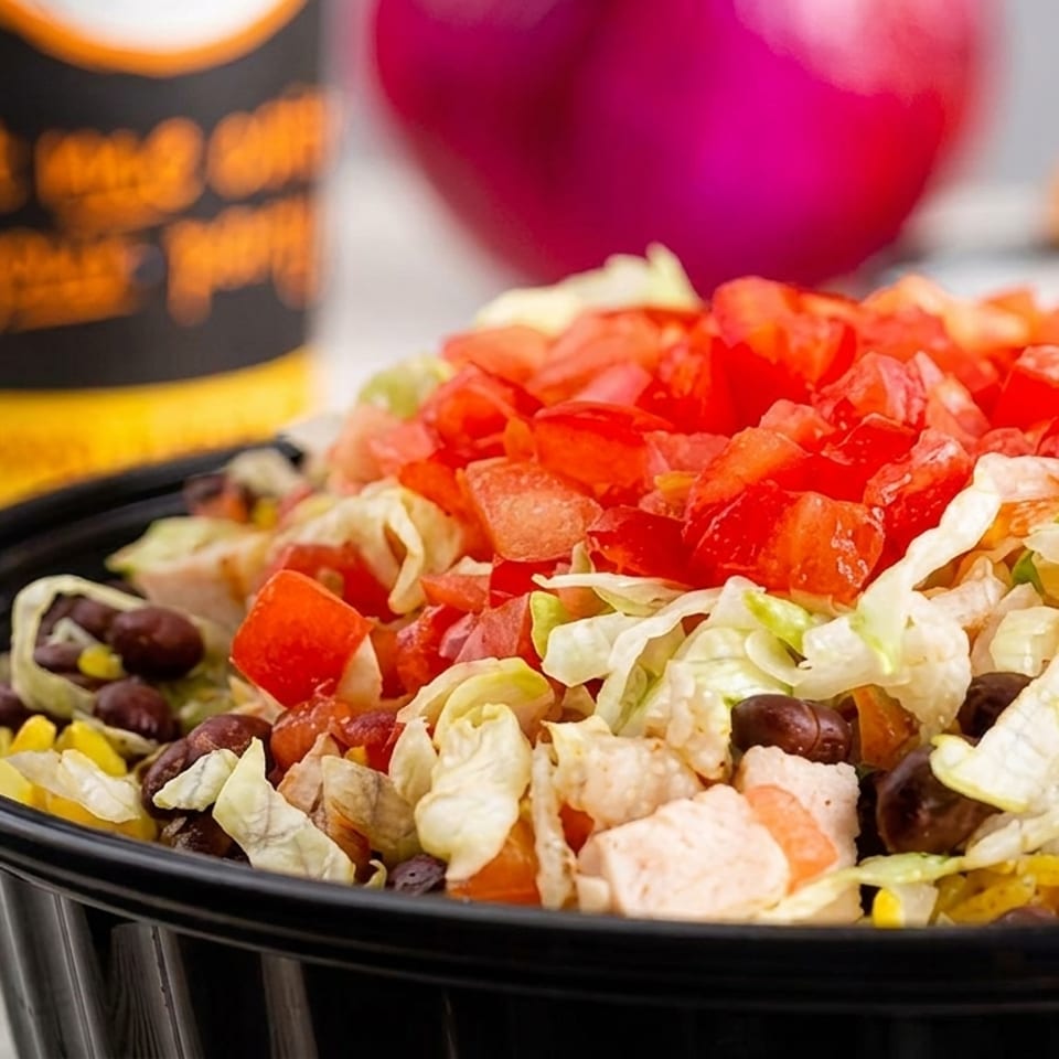 A close-up of a salad bowl filled with lettuce, diced tomatoes, black beans, corn, and chicken.