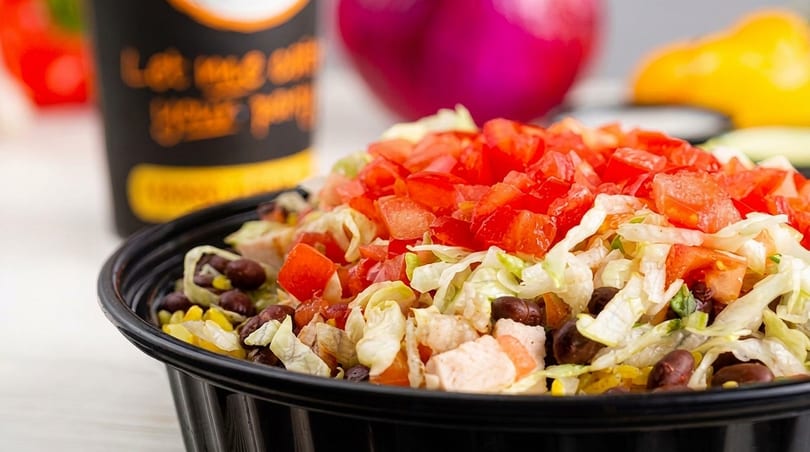 A close-up of a salad bowl filled with lettuce, diced tomatoes, black beans, corn, and chicken.