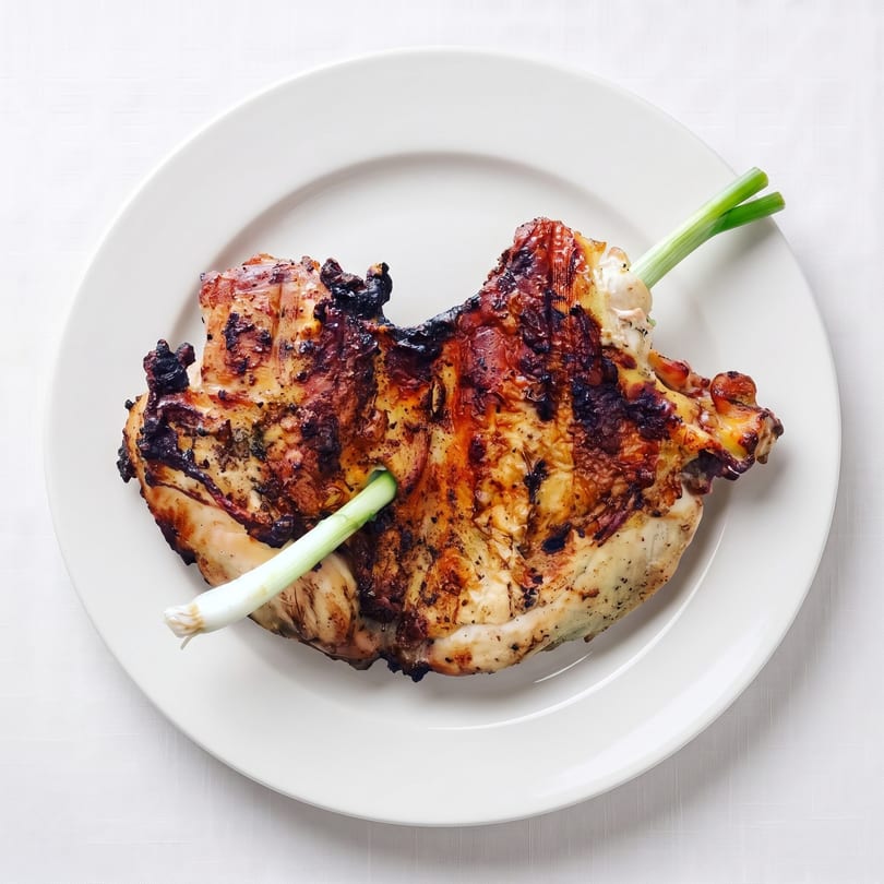Grilled chicken with crispy skin and a green onion garnish on a white plate.