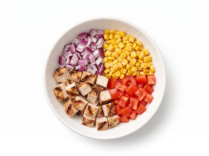 A white bowl containing diced grilled chicken, red onion, corn, and tomatoes.